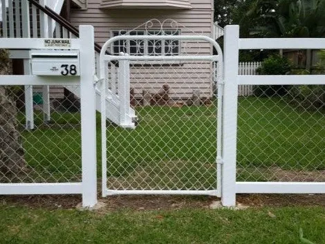 White chain-wire pedestrian gate with scroll top between white timber fence panels beside a letterbox