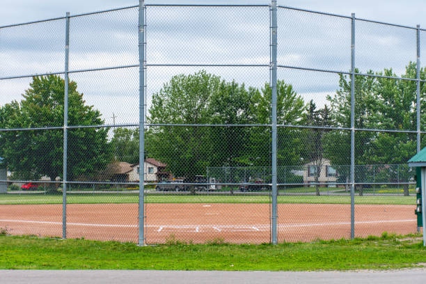 Tall chain-wire backstop fencing behind home plate on a softball diamond in a suburban park